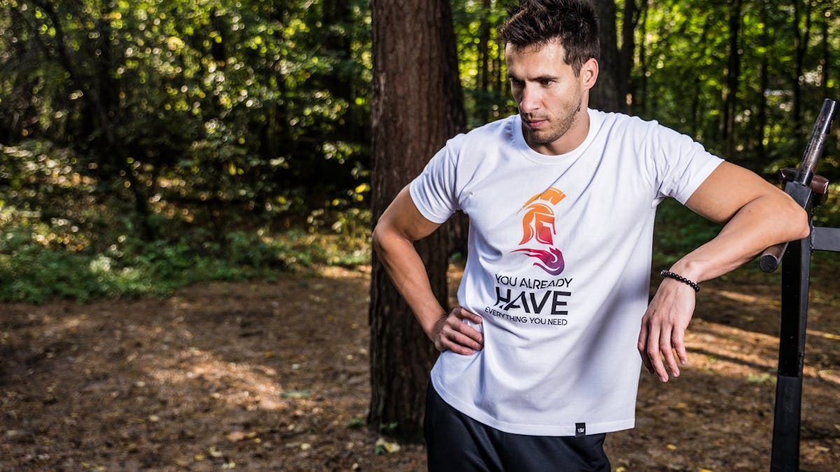 Man in forest wearing casual t-shirt, resting during outdoor workout.